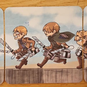Puede incluir: Un conjunto de tres tarjetas cuadradas con ilustraciones de dibujos animados de personajes de la serie de anime Attack on Titan. Los personajes se muestran en acci&oacute;n, con espadas y uniformes militares, sobre un fondo de cielo azul.
