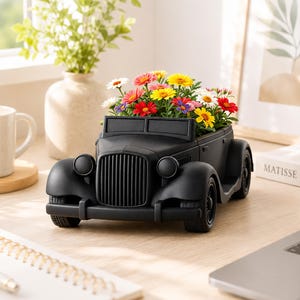 Könnte beinhalten: Ein mattschwarzer Übertopf in Form eines Oldtimers, gefüllt mit einem lebendigen Arrangement aus mehrfarbigen, gänseblümchenartigen Blumen in Rot, Gelb, Weiß und Violett. Der Übertopf zeigt einen detaillierten Kühlergrill, runde Scheinwerfer und Kotflügel.
