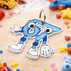 May include: A blue number six keychain with cartoon-like features, including eyes, arms, and legs. The keychain is surrounded by colorful toys, including a yellow car, a blue airplane, and various star and heart-shaped decorations.