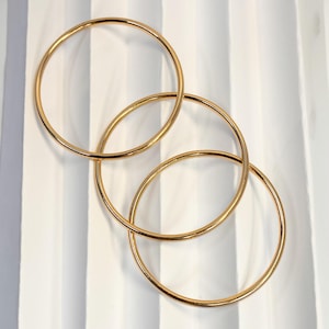 May include: Three gold-colored metal hoop earrings, interlocked in a decorative arrangement. The hoops are circular and have a smooth, polished finish. The background is a white and gray striped pattern.