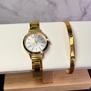May include: A gold watch with a silver face and a matching gold bracelet. The watch has a quartz movement and a rectangular link band. The bracelet is engraved with the word "LOVE".