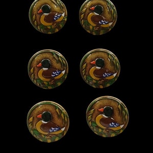 May include: Six round, brown, green, and yellow buttons with a painted image of a duck in a leafy setting.