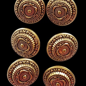 Könnte beinhalten: Sechs goldfarbene Metallknöpfe mit komplizierten kreisförmigen Designs. Jeder Knopf hat eine erhabene Mitte mit einem kleineren Kreis und einem dekorativen Muster am Rand.