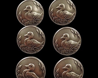 May include: Six silver-toned metal buttons with a raised design of a duck in a pond setting.