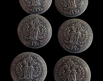May include: Six silver-coloured coins with a coat of arms featuring a double-headed eagle and the text "BURG CO TYR 1780 X ARCHID AVST DUX" around the edge.
