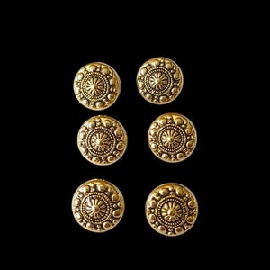 Peut inclure: Six boutons en métal couleur or avec un motif décoratif. Chaque bouton a un centre surélevé avec un motif circulaire et un cercle plus petit au centre.