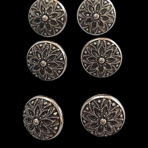 Può includere: Sei orecchini rotondi argentati con un design floreale. Ogni orecchino presenta un motivo floreale intricato in rilievo con un piccolo pezzo centrale rotondo.