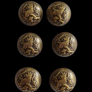 May include: Six antique brass buttons, each featuring a detailed embossed design of a crowned lion holding a sword. The round buttons have a tarnished, aged appearance, suggesting they are vintage or vintage-inspired.