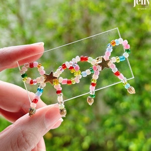 May include: A colourful beaded bow with gold star accents and dangling beads. The bow is displayed on a clear surface.