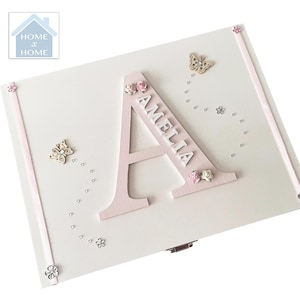 Peut inclure: Un coffret en bois blanc avec un grand "A" rose et le nom "AMELIA" en blanc. La bo&icirc;te est d&eacute;cor&eacute;e de papillons, de fleurs et de petits accents argent&eacute;s. Le logo Home x Home est visible en haut &agrave; gauche.