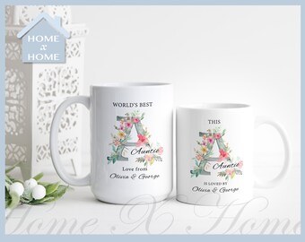 Può includere: Due tazze in ceramica bianca con un design floreale con la lettera A. La tazza a sinistra dice "World's Best Auntie Love from Olivia & George". La tazza a destra dice "This Auntie is loved by Olivia & George".