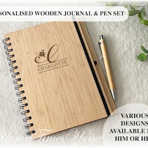 May include: A personalised wooden journal and pen set. The journal has a spiral binding and is made of light brown wood. The cover is engraved with the letter "C" and the name "CHARLOTTE". The pen is also made of wood and has a silver tip.