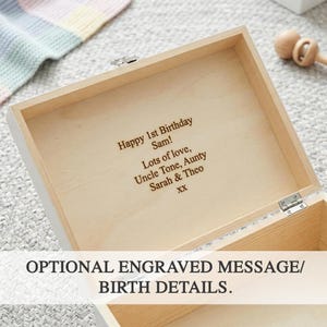 Peut inclure: Une bo&icirc;te en bois blanche avec un int&eacute;rieur de couleur claire. La bo&icirc;te est ouverte, r&eacute;v&eacute;lant un message grav&eacute; qui se lit "Happy 1st Birthday Sam! Lots of love, Uncle Tone, Aunty Sarah & Theo XX." Le texte "OPTIONAL ENGRAVED MESSAGE/ BIRTH DETAILS" est &eacute;galement visible.