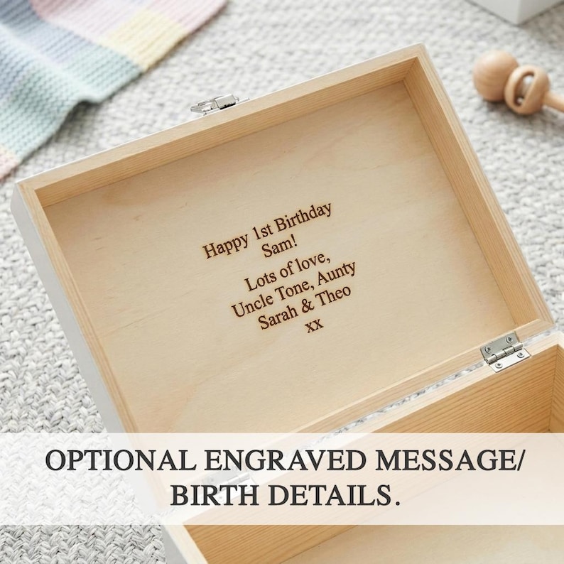 Peut inclure: Une bo&icirc;te en bois blanche avec un int&eacute;rieur de couleur claire. La bo&icirc;te est ouverte, r&eacute;v&eacute;lant un message grav&eacute; qui se lit "Happy 1st Birthday Sam! Lots of love, Uncle Tone, Aunty Sarah & Theo XX." Le texte "OPTIONAL ENGRAVED MESSAGE/ BIRTH DETAILS" est &eacute;galement visible.
