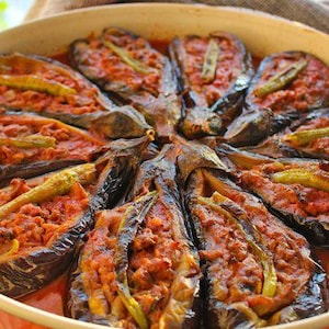 Könnte beinhalten: Nahaufnahme einer Schale mit Auberginen, gefüllt mit Hackfleisch und grünen Paprikaschoten, übergossen mit Tomatensauce. Die Schale befindet sich in einer weißen Keramik-Backform.