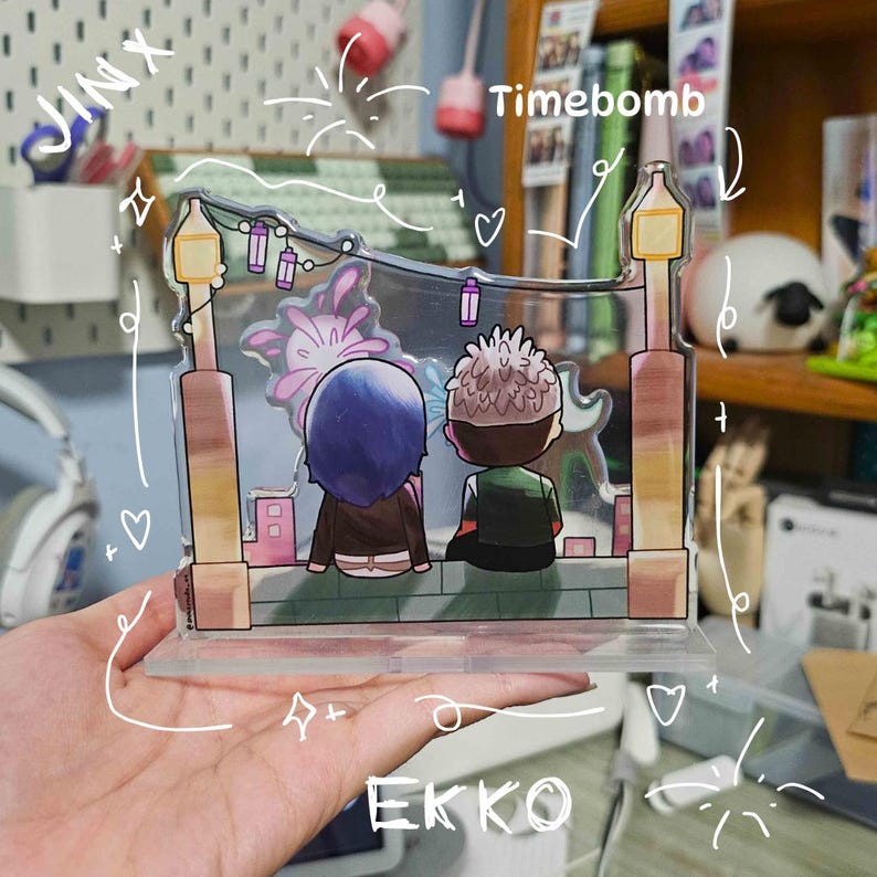 May include: A clear acrylic stand featuring an anime-style illustration of two figures seated on a ledge, with a cityscape backdrop. The stand has two lamp post designs on each side. The text "Timebomb" is visible.