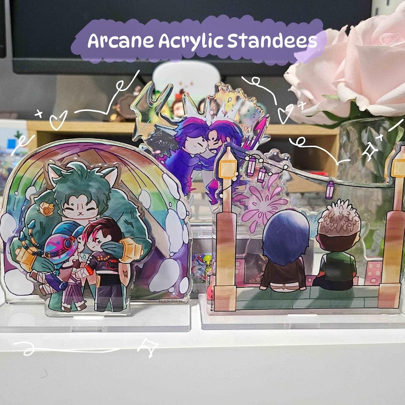 May include: Acrylic standees featuring colorful cartoon characters in various scenes. One standee depicts a group of characters under a rainbow, while another shows two figures kissing. The text "Arcane Acrylic Standees" is visible.