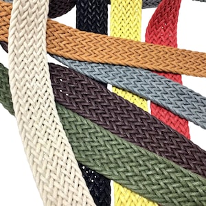 Könnte beinhalten: Nahaufnahme einer Sammlung geflochtener Gürtel in verschiedenen Farben, darunter Creme, Beige, Schwarz, Gelb, Rot und Grün. Die Gürtel bestehen aus einem gewebten Material und werden vor einem weißen Hintergrund präsentiert.