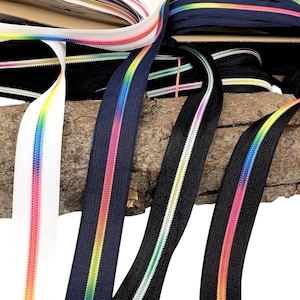 Könnte beinhalten: Sortiment an farbenfrohem Reißverschlussband mit Regenbogenstreifen. Das Band ist schwarz, weiß und marineblau. Das Band ist um ein Stück Holz gewickelt.