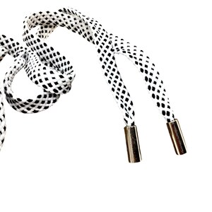 Könnte beinhalten: Nahaufnahme von weiß-schwarz gemusterten Schnürsenkeln mit metallischen Ösen. Die Schnürsenkel bestehen aus einem gewebten Material mit einem sich wiederholenden schwarzen Rautenmuster. Die Ösen sind silberfarben glänzend.