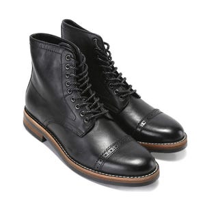 May include: A pair of black leather boots with a cap toe design and lace-up closure. The boots have a brown sole with a white stitch detail. The boots are a classic style.