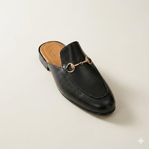 Puede incluir: Mule de cuero negro con detalle de adorno de caballo en metal dorado. El zapato tiene una punta redondeada y un tac&oacute;n bajo. El interior es de color marr&oacute;n claro. La marca "Gucci" es visible dentro del zapato.