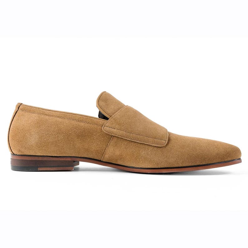 Puede incluir: Mocas&iacute;n de ante marr&oacute;n claro. El zapato tiene un dise&ntilde;o sin cordones, una puntera redondeada y una correa en el empeine. Presenta una suela marr&oacute;n. Un estilo cl&aacute;sico, adecuado para vestimenta formal o informal. Mide unos 28 cm de largo.