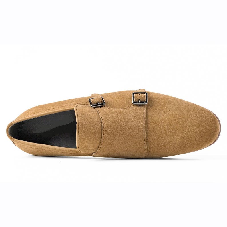 Puede incluir: Zapato de doble hebilla de ante color canela con dos hebillas plateadas. El zapato tiene una puntera redondeada y un dise&ntilde;o liso. La suela es de un tono marr&oacute;n m&aacute;s oscuro.