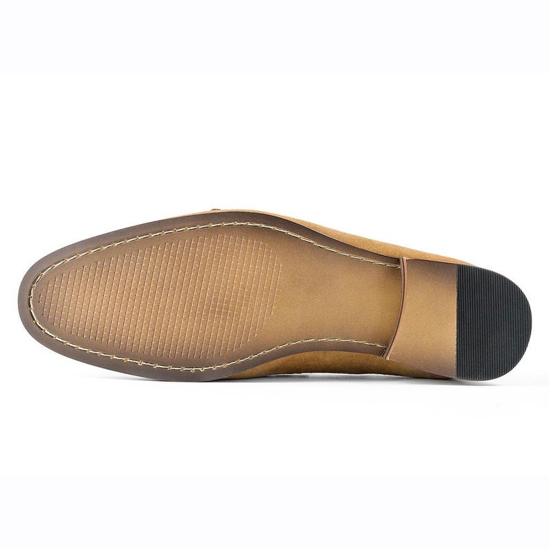 Puede incluir: Vista inferior de un mocas&iacute;n de ante color canela. La suela es de color marr&oacute;n claro con un patr&oacute;n texturizado y un tac&oacute;n marr&oacute;n oscuro. El zapato est&aacute; cosido con hilo de color claro.