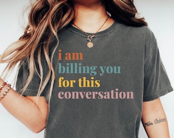 May include: A gray t-shirt with the text "i am billing you for this conversation" in colorful letters. The text is in a casual, handwritten font.