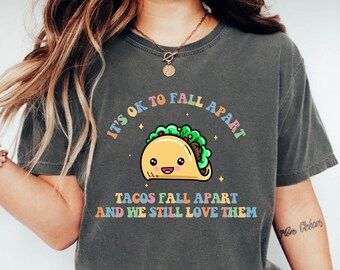 May include: A gray t-shirt with a cartoon taco graphic and the text "It's ok to fall apart. Tacos fall apart and we still love them."