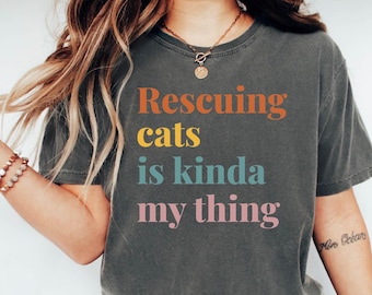 May include: A dark gray t-shirt with the text "Rescuing cats is kinda my thing" printed in rainbow colors.