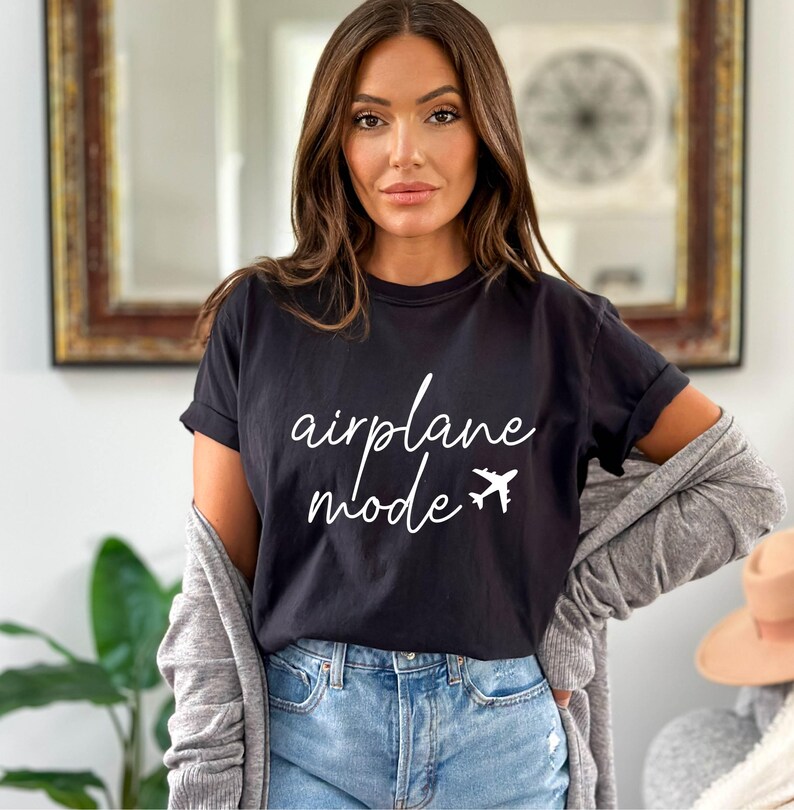 Op de afbeelding: Een zwart T-shirt met witte tekst die "vliegtuigmodus" zegt en een kleine vliegtuigafbeelding.