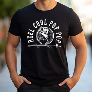 May include: Black t-shirt featuring a white graphic of a fish jumping out of the water with the text "Reel Cool Pop Pop" around it.