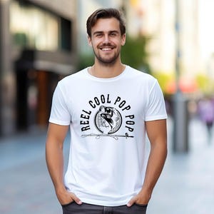 May include: White t-shirt with a black graphic of a fish jumping out of the water with the text "Reel Cool Pop Pop" around it.