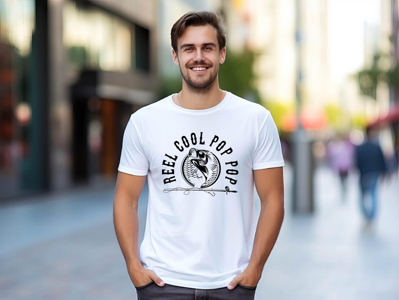 May include: White t-shirt with a black graphic of a fish jumping out of the water with the text "Reel Cool Pop Pop" around it.