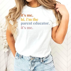 Pu&ograve; includere: T-shirt bianco con la scritta "it's me, hi. I'm the parent educator, it's me." in un gradiente di colori. La maglietta &egrave; abbinata a jeans di denim blu chiaro. Lo stile &egrave; casual e confortevole.