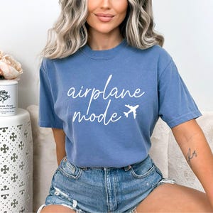 Op de afbeelding: Een blauw t-shirt met de tekst "airplane mode" in witte letters en een klein vliegtuigicoon.