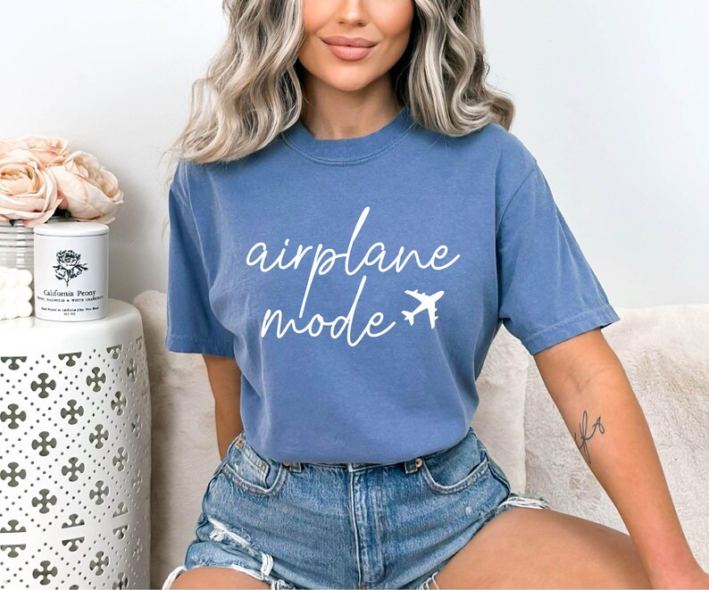 Op de afbeelding: Een blauw t-shirt met de tekst "airplane mode" in witte letters en een klein vliegtuigicoon.