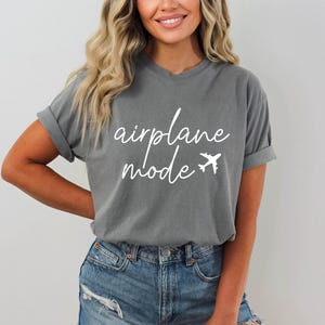 Op de afbeelding: Een grijs T-shirt met de tekst "airplane mode" in witte cursieve letters en een wit vliegtuigpictogram.