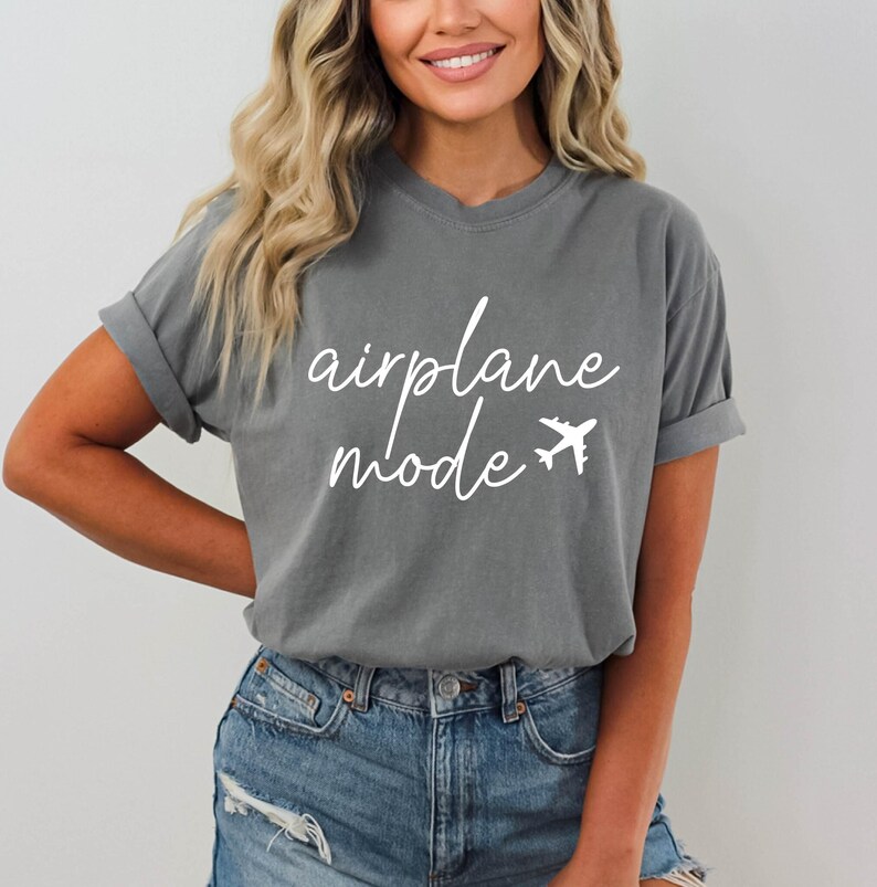 Op de afbeelding: Een grijs T-shirt met de tekst "airplane mode" in witte cursieve letters en een wit vliegtuigpictogram.