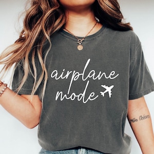 Op de afbeelding: Een donkergrijs T-shirt met de tekst "airplane mode" in witte letters en een kleine vliegtuigafbeelding.