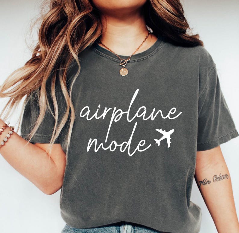 Op de afbeelding: Een donkergrijs T-shirt met de tekst "airplane mode" in witte letters en een kleine vliegtuigafbeelding.