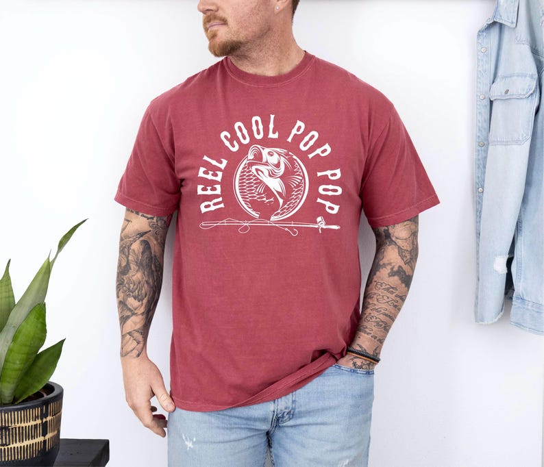 May include: A red t-shirt with a white graphic of a fish with the text "Reel Cool Pop Pop" around it.