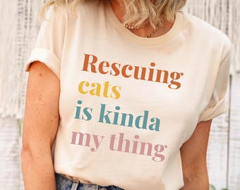 May include: A white t-shirt with the text "Rescuing cats is kinda my thing" printed in colorful letters.