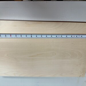 May include: A close-up of a light wood board with a tape measure across the top. The tape measure reads 18 inches.