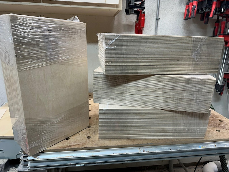 May include: A stack of four sheets of plywood wrapped in plastic, with one sheet standing upright next to the stack.