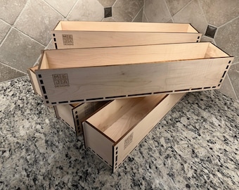 May include: A stack of three rectangular wooden boxes with a light wood finish. The boxes have a simple design with a logo that reads "ME JA DESIGNS" on the side. The boxes are stacked on top of each other.