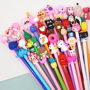 May include: A collection of colorful pens with various cute animal and character toppers. The toppers include a unicorn, a donut, a penguin, a mermaid, a dinosaur, a snowman, a flamingo, a reindeer, a cat, a panda, a star, a llama, a cactus, a mushroom, a whale, a Christmas tree, a gnome, a sushi, a pineapple, a rabbit, a bear, an owl, a bird, and a fish.