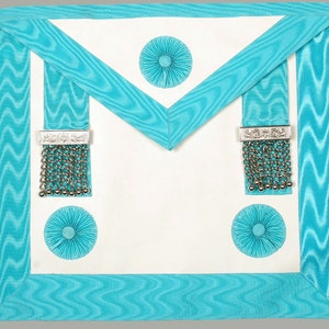 May include: A white Masonic apron with a turquoise blue border and fringe. The apron has three turquoise blue rosettes and two silver tassels.